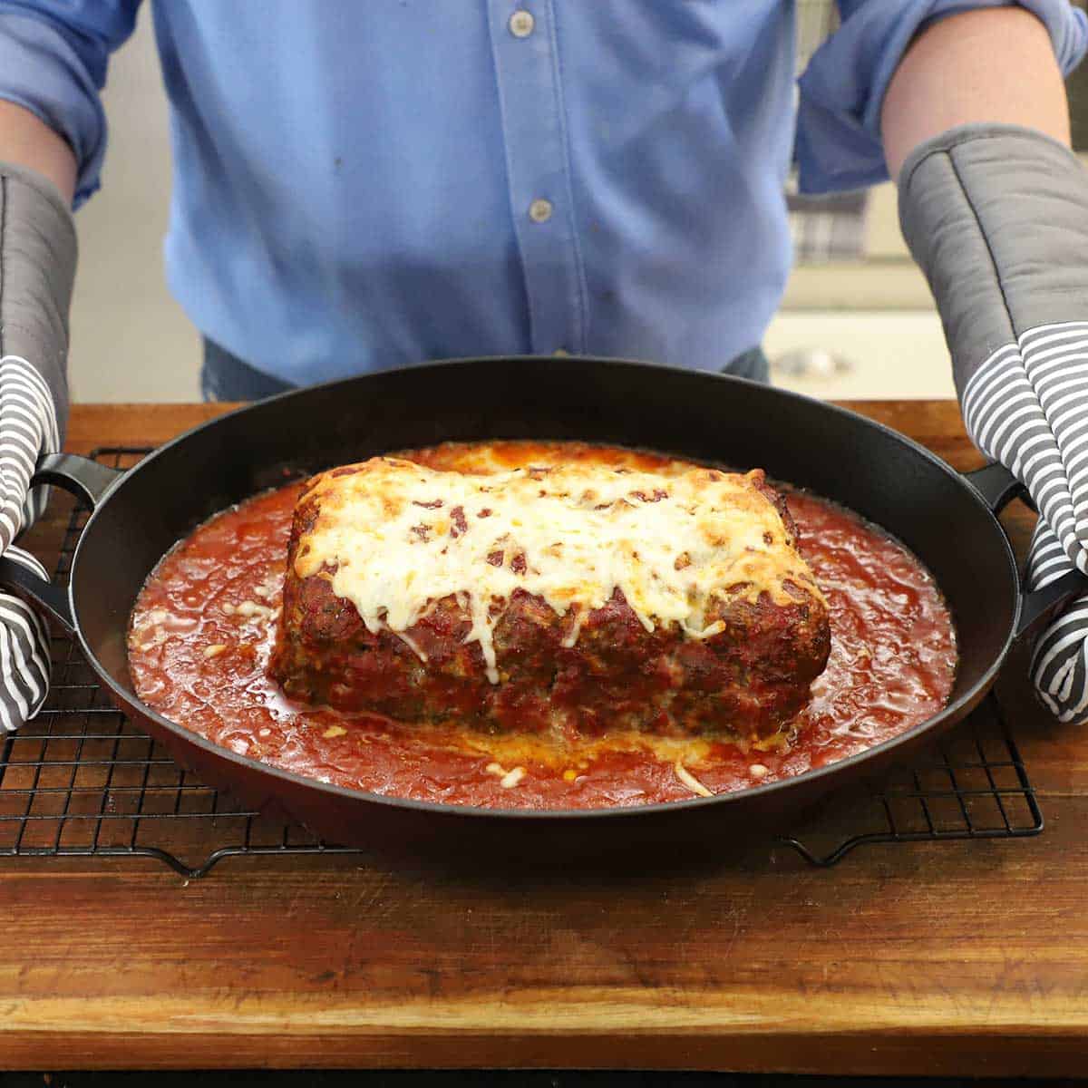 A person holding a baking dish that is filled with The Best Juicy Italian Meatloaf with Marinara Glaze.