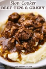 A close-up view of a shallow white bowl filled with a serving of slow cooker beef tips and gravy over a pile of mashed potatoes.