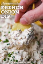 A person holding a potato chip that has a mound of homemade French onion dip on it over a bowl of the dip.