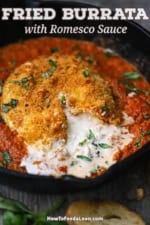 A crispy fried Burrata ball of cheese that has been broken open with creamy cheese drizzling out into a skillet that has Romesco sauce in it.