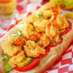 A close-up view of a New Orleans Fried Shrimp Po-Boy sandwich in a red plastic basket lined with red and white checkered wax paper.