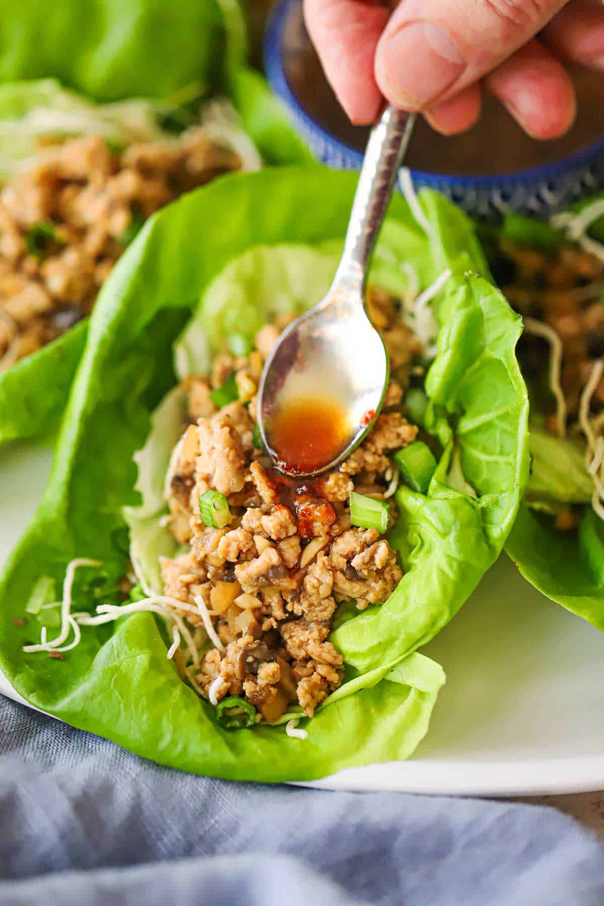 A person using a small spoon to drizzle a spicy red sauce over the top of a copycat P.F. Chang Chicken Lettuce Wrap.