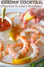 A person squeezing a lemon wedge over a plate filled with Classic Jumbo Shrimp Cocktail.