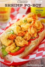 A close-up view of a New Orleans Fried Shrimp Po-Boy sandwich in a red plastic basket lined with red and white checkered wax paper.