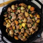 An overhead view of Garlic Butter Steak Bites and Potatoes in a large black cast-iron skillet garnished with chopped Italian parsley and coarse sea salt.