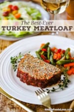 A thick slice of juicy turkey meatloaf resting on a white dinner plate with a pile of steamed vegetables next to it.