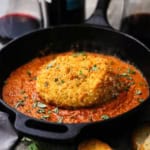 A close-up view of a whole crispy fried burrata that is resting on a bed of smokey romesco sauce in a black cast-iron skillet.