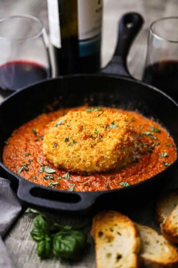 A straight-on view of a whole crispy fried burrata that is resting on a bed of smokey romesco sauce in a black cast-iron skillet.
