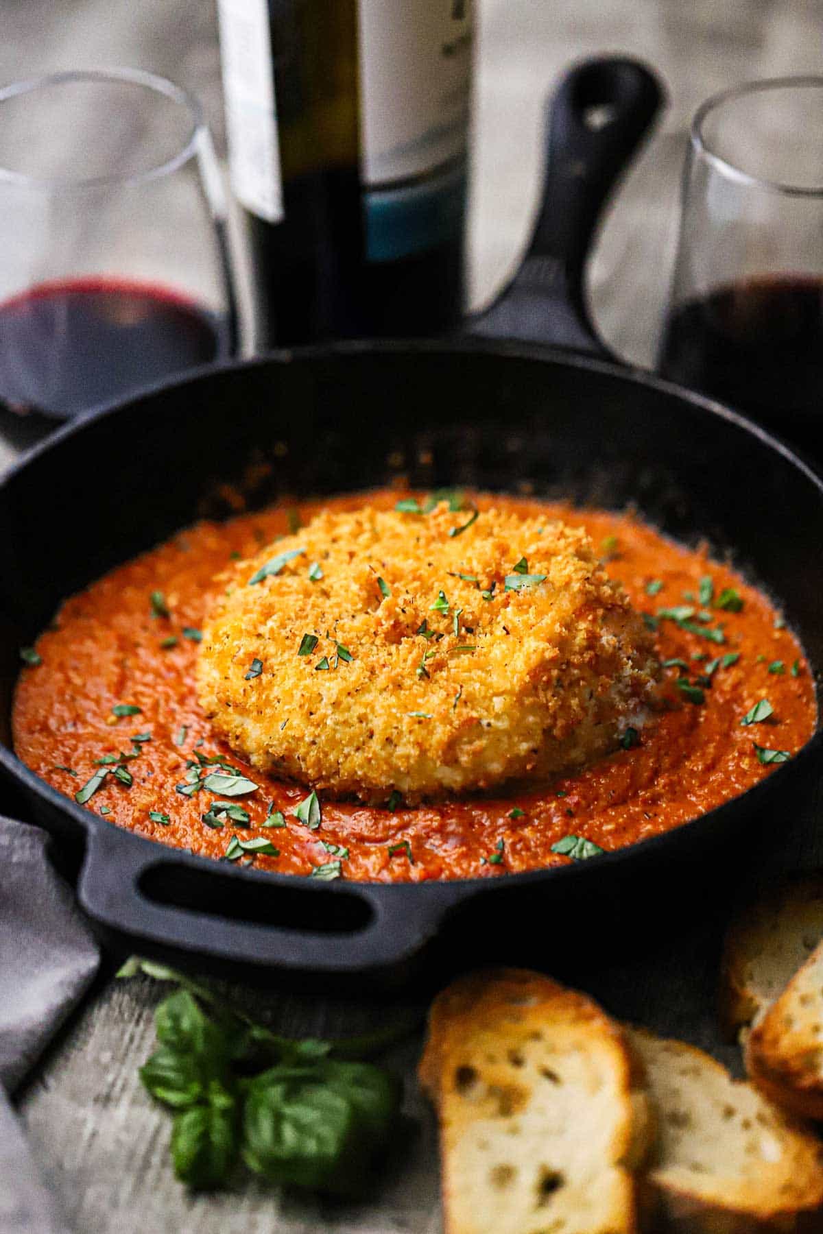 A straight-on view of a whole crispy fried burrata that is resting on a bed of smokey romesco sauce in a black cast-iron skillet.