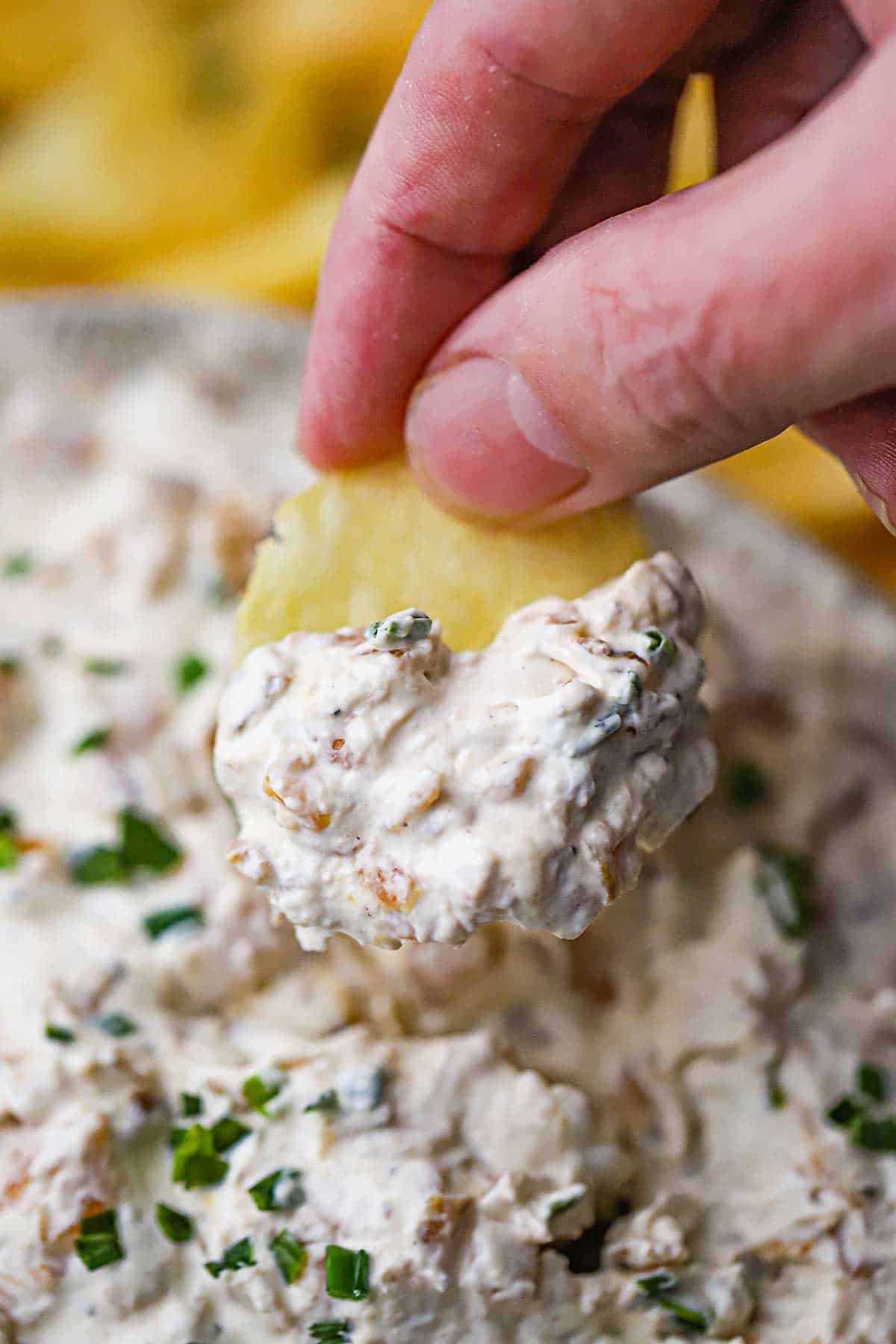 A person holding a potato chip that has a mound of homemade French onion dip on it over a bowl of the dip.