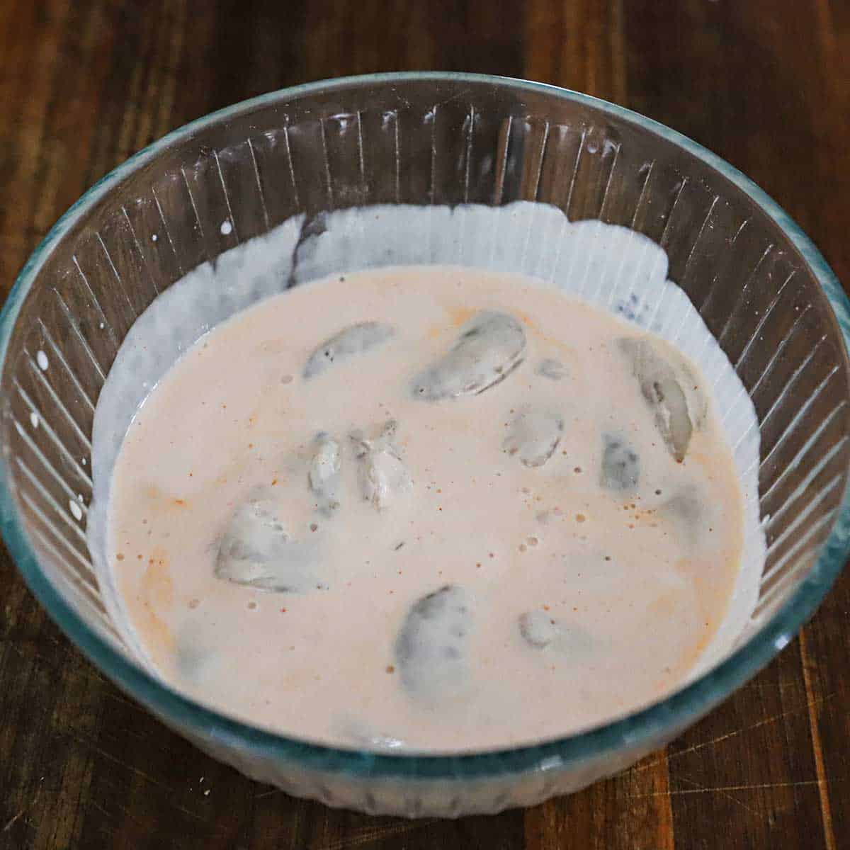 A glass bowl filled with raw Gulf shrimp soaking in a mixture of buttermilk and hot sauce.