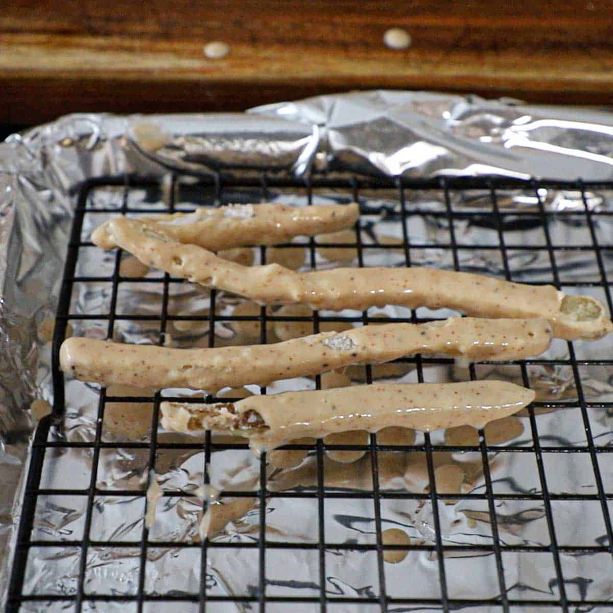 Four partially fried French fries that have been coated with flour and then a beer batter and are resting on a baking rack over a foil-lined baking pan.