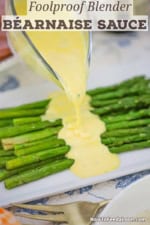 A person pouring blender Béarnaise sauce from a glass gravy boat of a pile of pan-seared asparagus on a white platter.