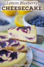 A person using a cake spatula to lift a slice of lemon blueberry cheesecake from a the cake resting on a circular white cake dish.