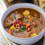 A bowl of classic Guinness beef stew in a white soup bowl and garnished with crispy bits of bacon and chopped Italian parsley.