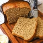 A close-up view of a loaf of deli-style rye bread that has two slices laying on a cutting board with the rest of the loaf behind them.