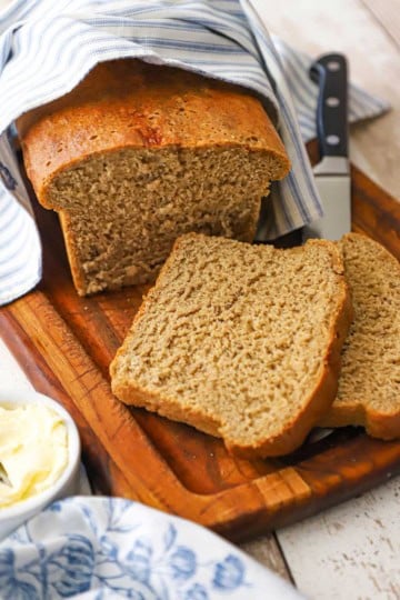 A close-up view of a loaf of deli-style rye bread that has two slices laying on a cutting board with the rest of the loaf behind them.