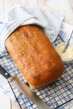 A Deli-Style Rye Sandwich Bread loaf on a wire baking rack over a colorful napkin.