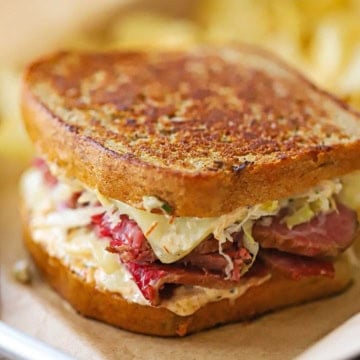 A close-up view of a "From Scratch" Reuben Sandwich resting on a brown paper in a small metal sheet pan.