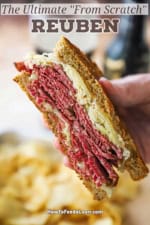 A person holding half of a "From Scratch" reuben sandwich revealing the stacks of corned beef, and the sauerkraut, melty cheese, surrounded by the toasty slices of rye bread.