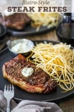 An up-close view of French Bistro-Style Steak Frites with a reverse-seared New York Strip steak on a plate next to a pile of shoestring French fries and a small vessel of garlic basil aioli.