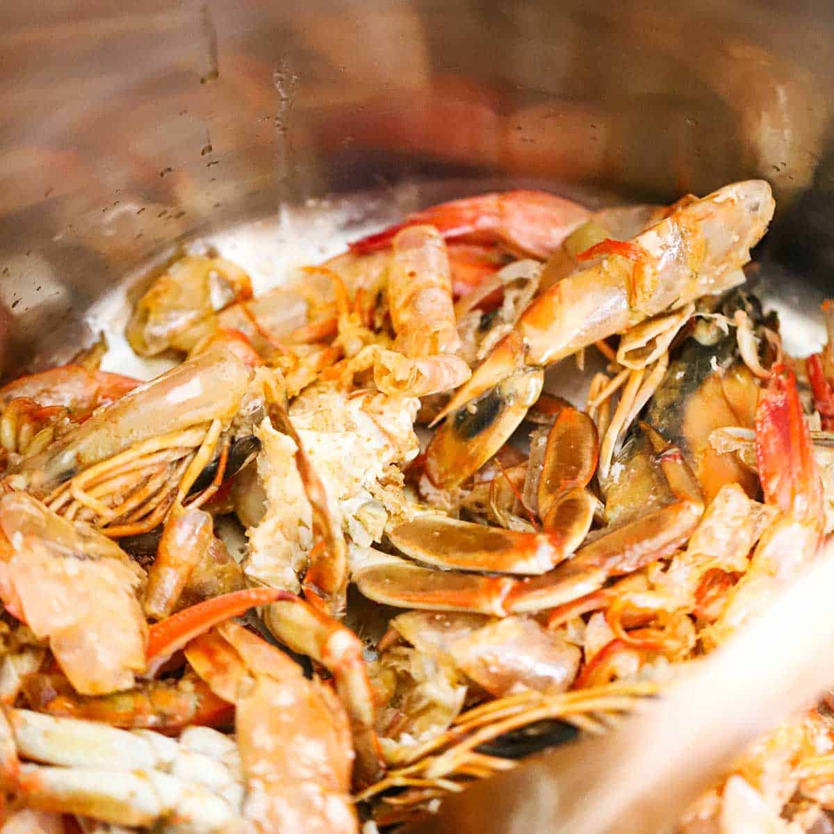A close-view of shellfish shells, tails, and legs that are being seared in a large stock pot.