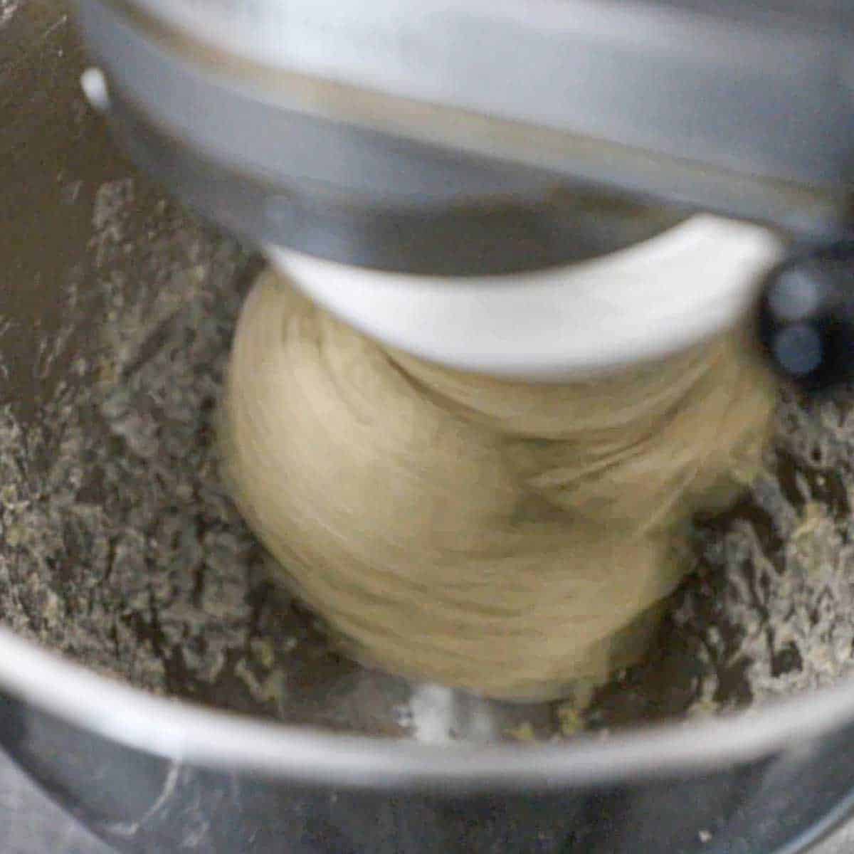 A view into the bowl of a stand-mixer with a ball of rye bread dough been mixed with a dough attachment and is not touching the sides of the bowl.