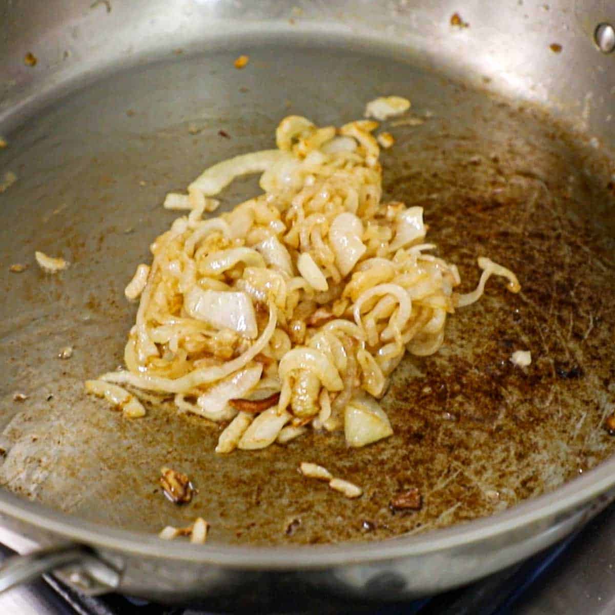 A pile of sautéed onions in the center of a large stainless steel skillet on a gas stove.