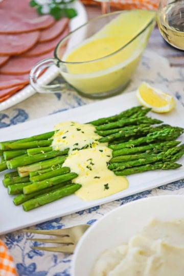 A rectangle white platter filled with Asparagus with Béarnaise Sauce with a glass gravy boat filled with the Béarnaise sauce.