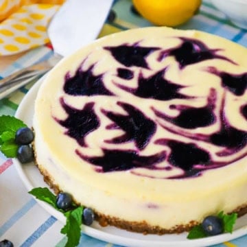 A close-up view of a lemon blueberry cheesecake with colorful blueberry-colored swirl designs on the top of the cake.