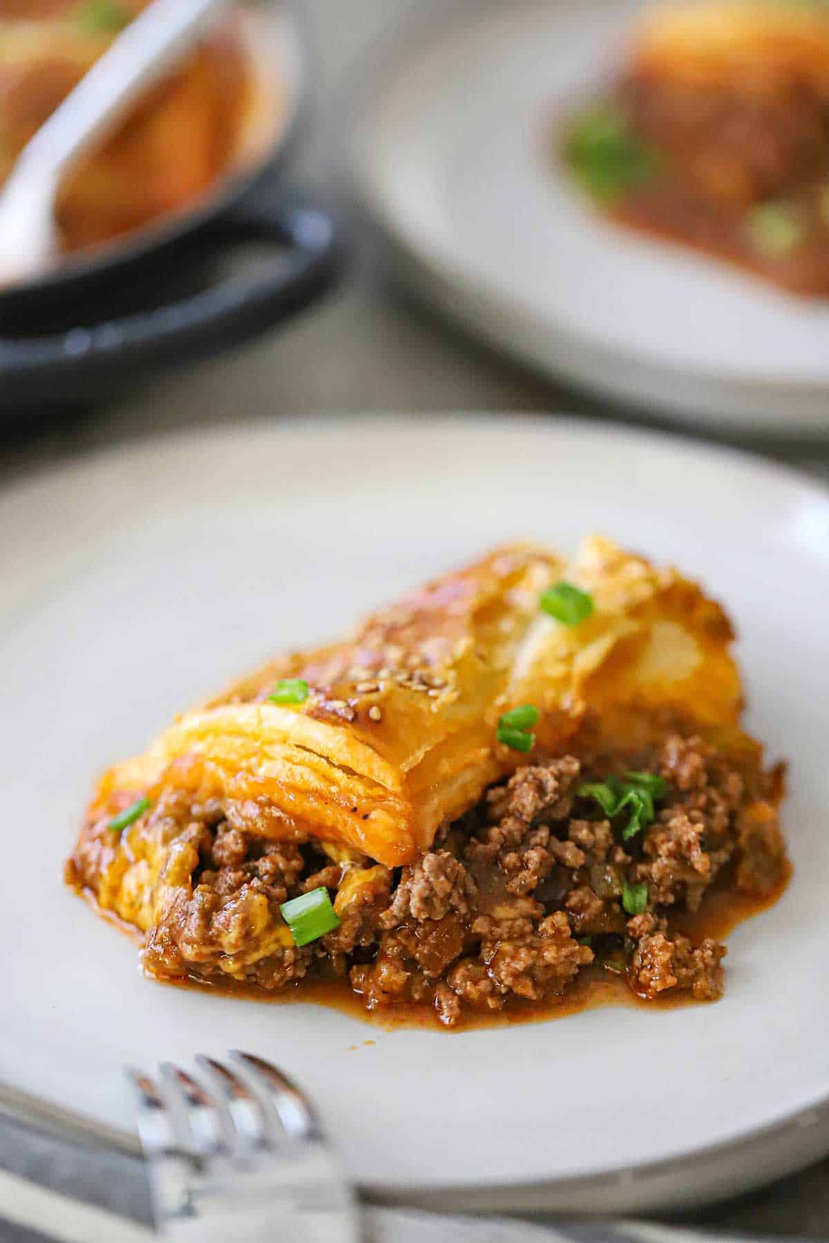 A close-up view of a serving of Sloppy Joe Casserole on a white dinner plate with a fork sitting nearby.