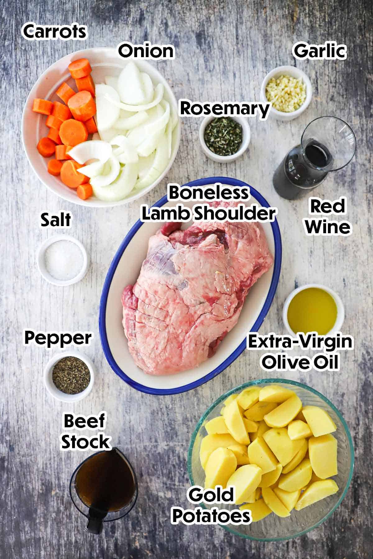 An arrangement of ingredients for slow-roasted lamb shoulder with crispy potatoes including a boneless lamb shoulder, gold potatoes, carrots, onion, garlic, red wine, oil, beef stock, and seasonings.