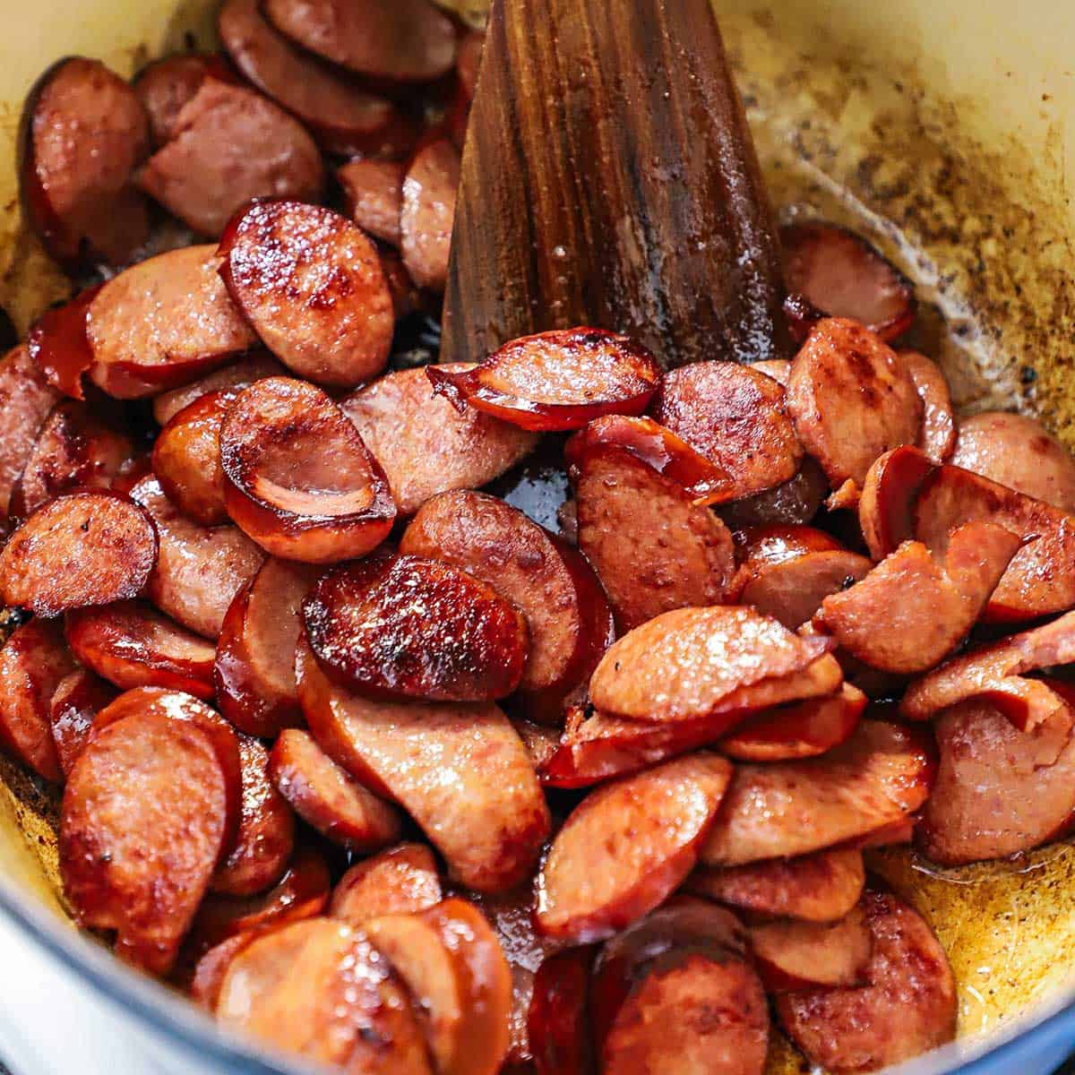 A close-up view of sliced kielbasa that is being sautéed in a large Dutch oven.