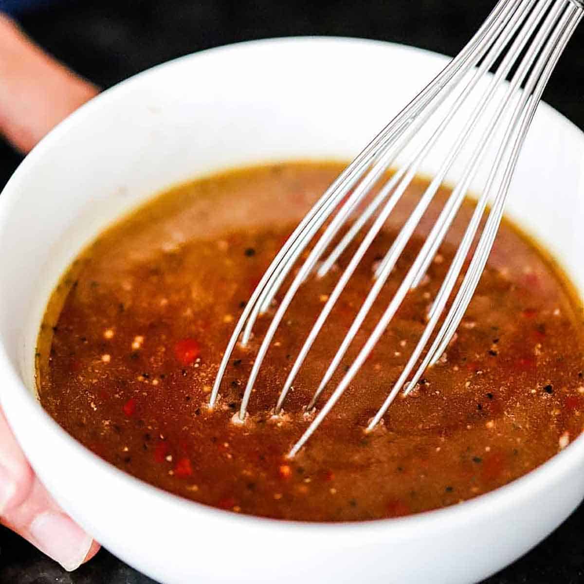 A close-up view of a person using a small whisk to combine the ingredients for a stir-fry sauce for sesame chicken.