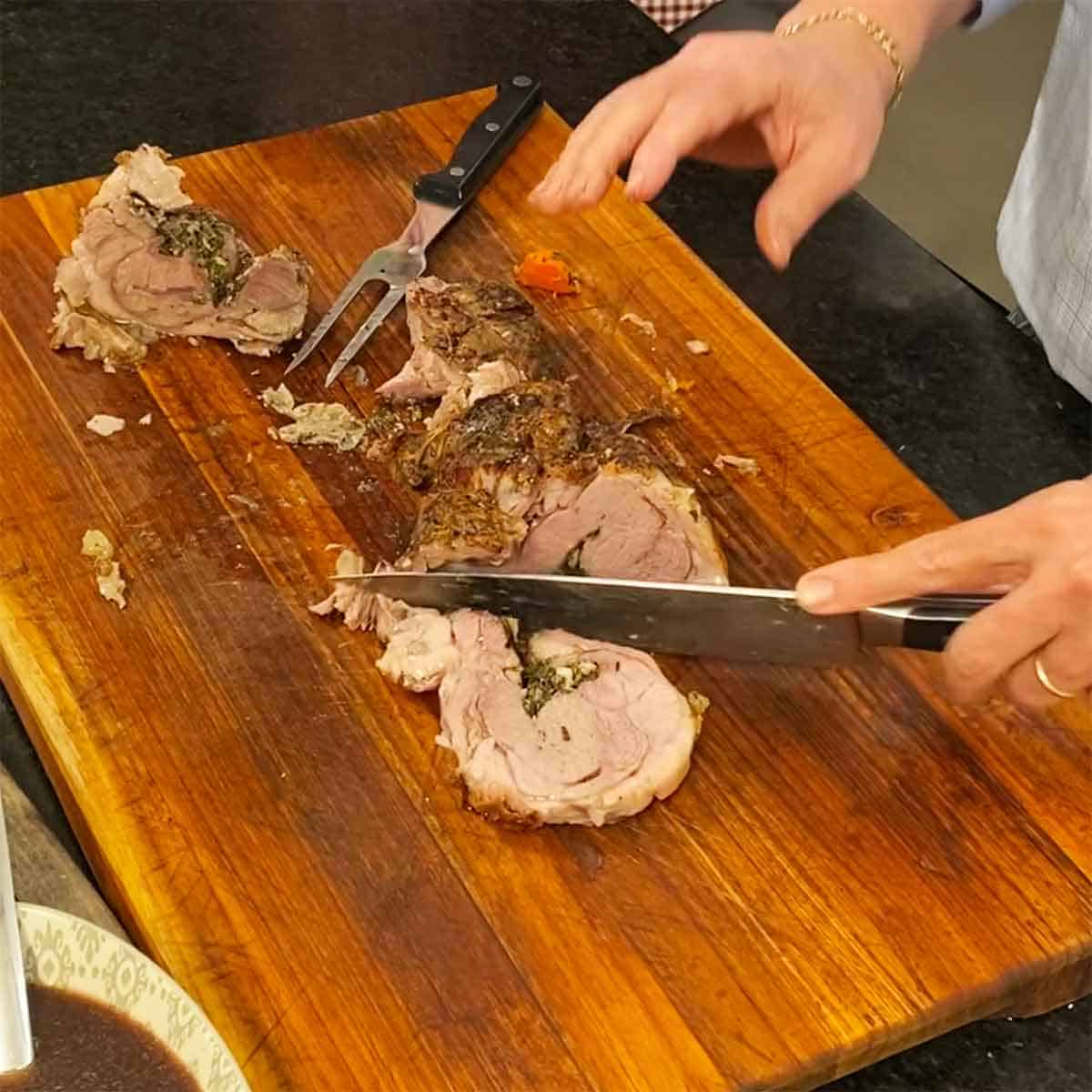 A person using a large chef's knife to slice a slow-roasted lamb shoulder on a wooden cutting board.