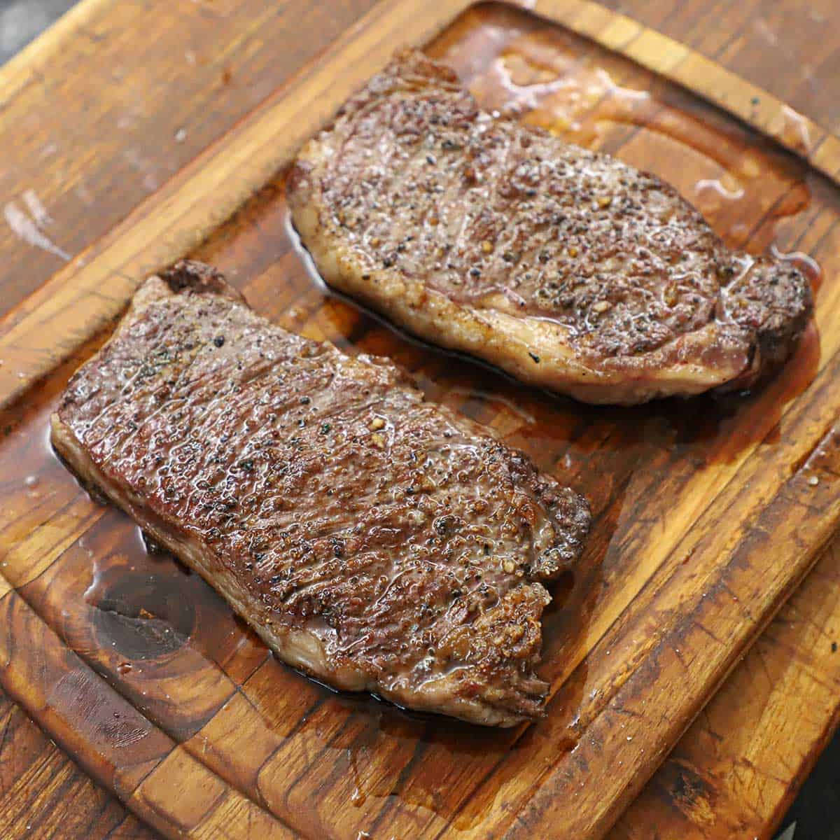 Two reverse-seared New York strip steaks resting on a wooden cutting board.
