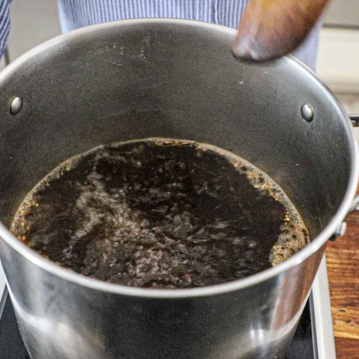 A person using a large wooden spoon to stir and curing brine to a boil on an induction oven.