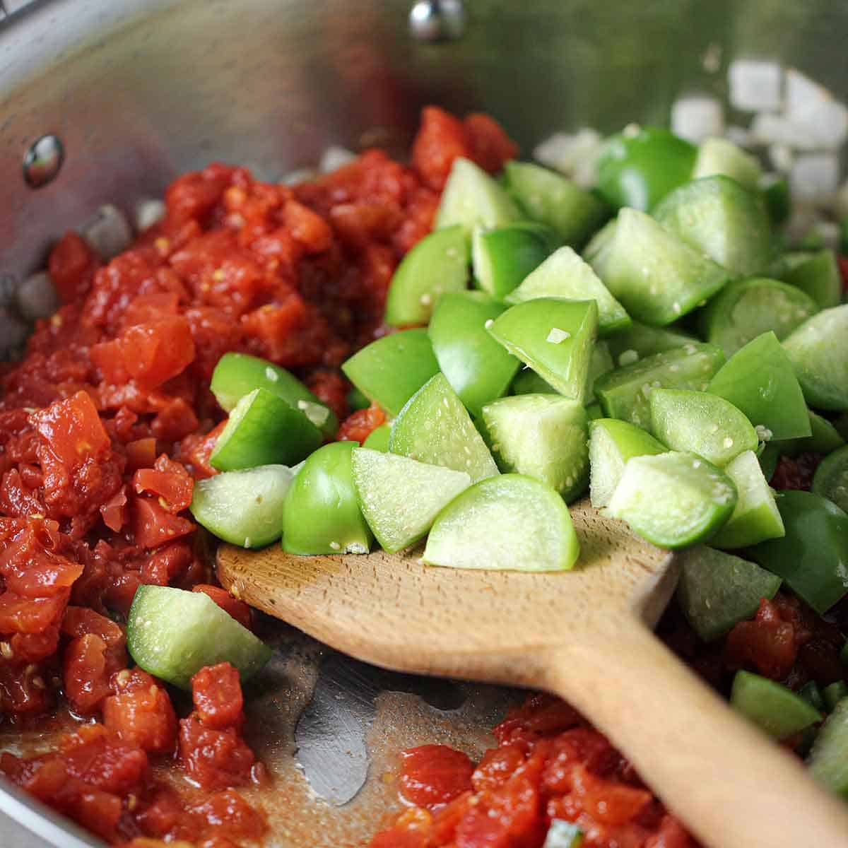 A person using a wooden spatula to stir quartered tomatillos and chopped tomatoes, or Ro-tel.