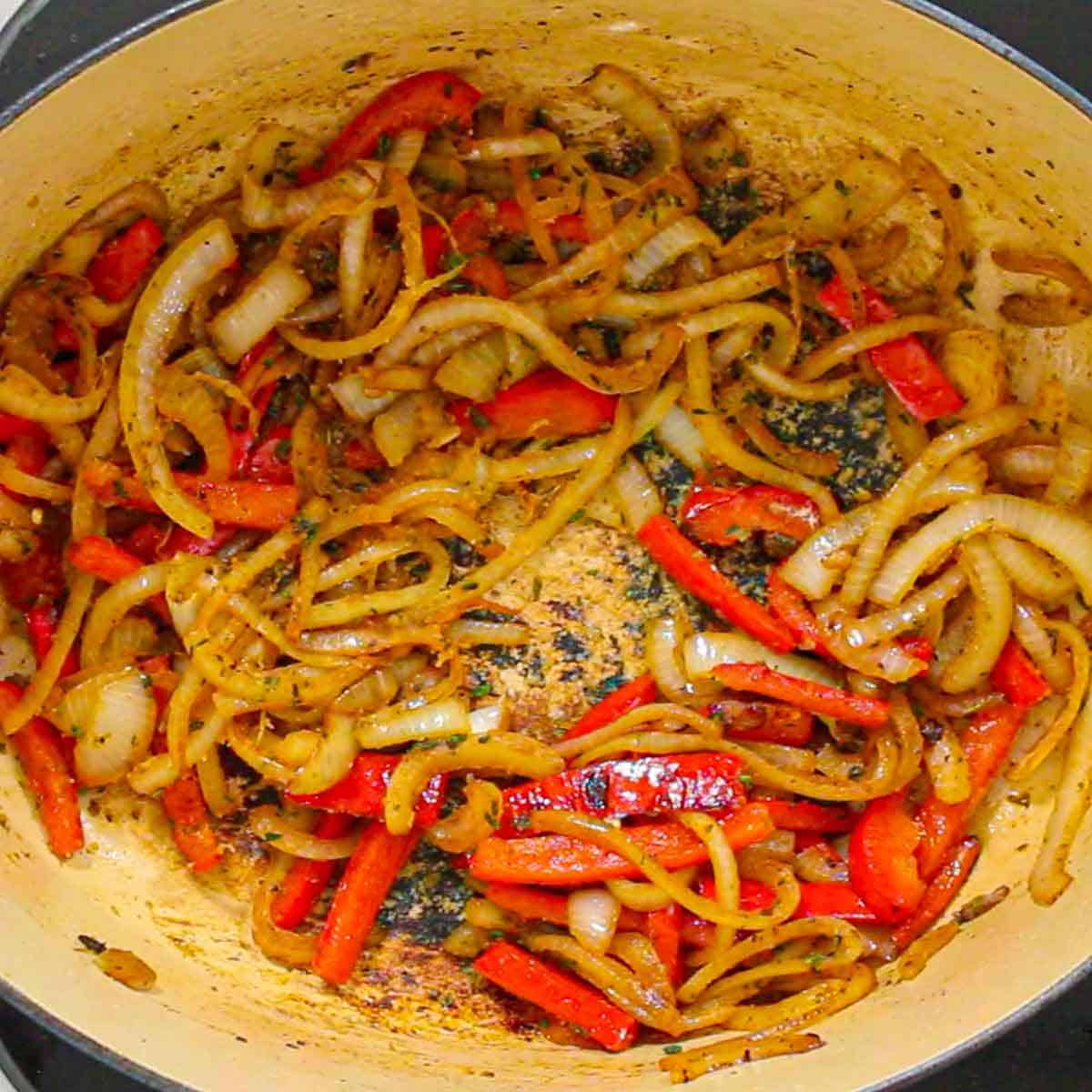 An overhead view of slices onions and red bell peppers that are being sautéed in a large Dutch oven.