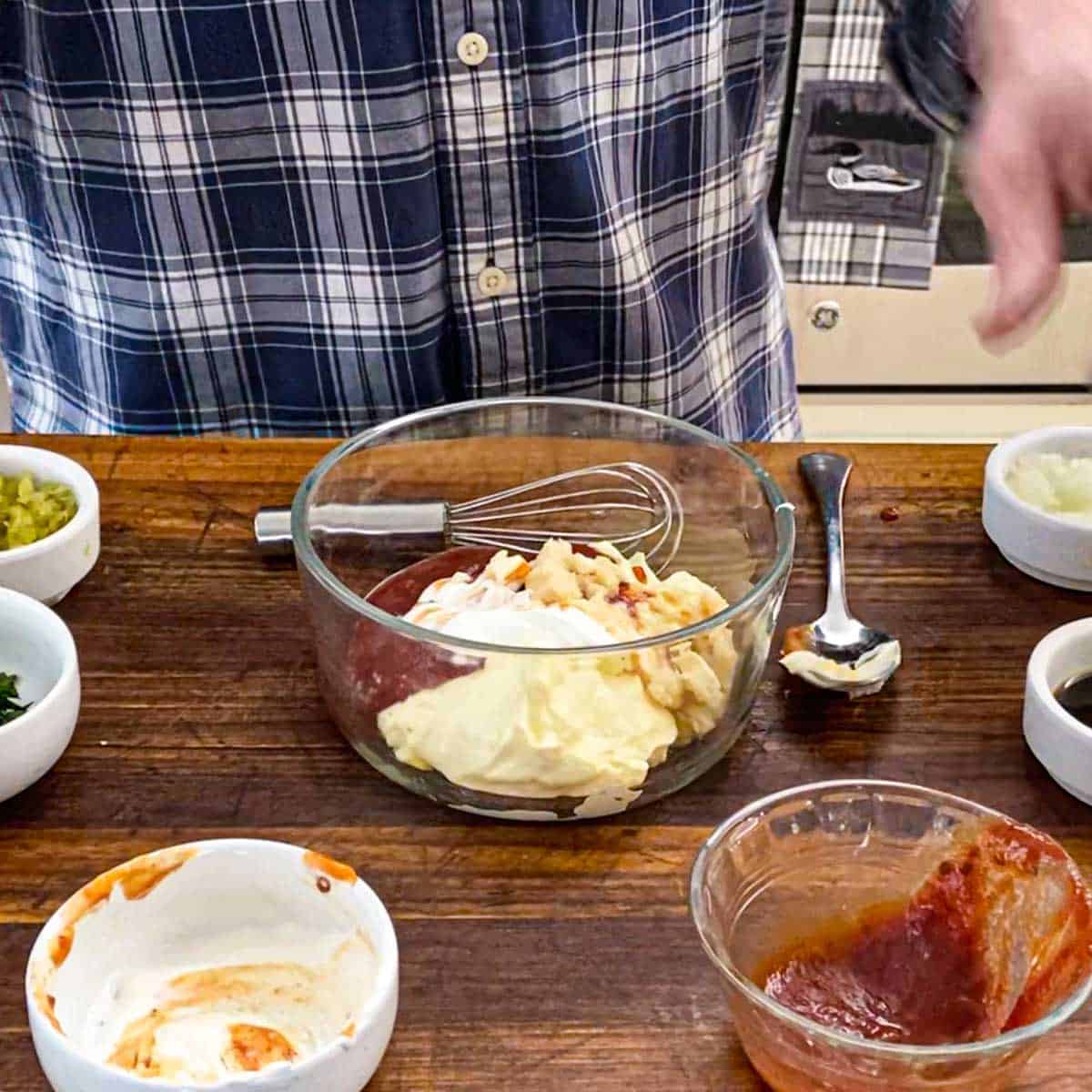 A person standing behind a small glass bowl filled with mayonnaise, chili sauce, sour cream, and prepared horseradish sauce.