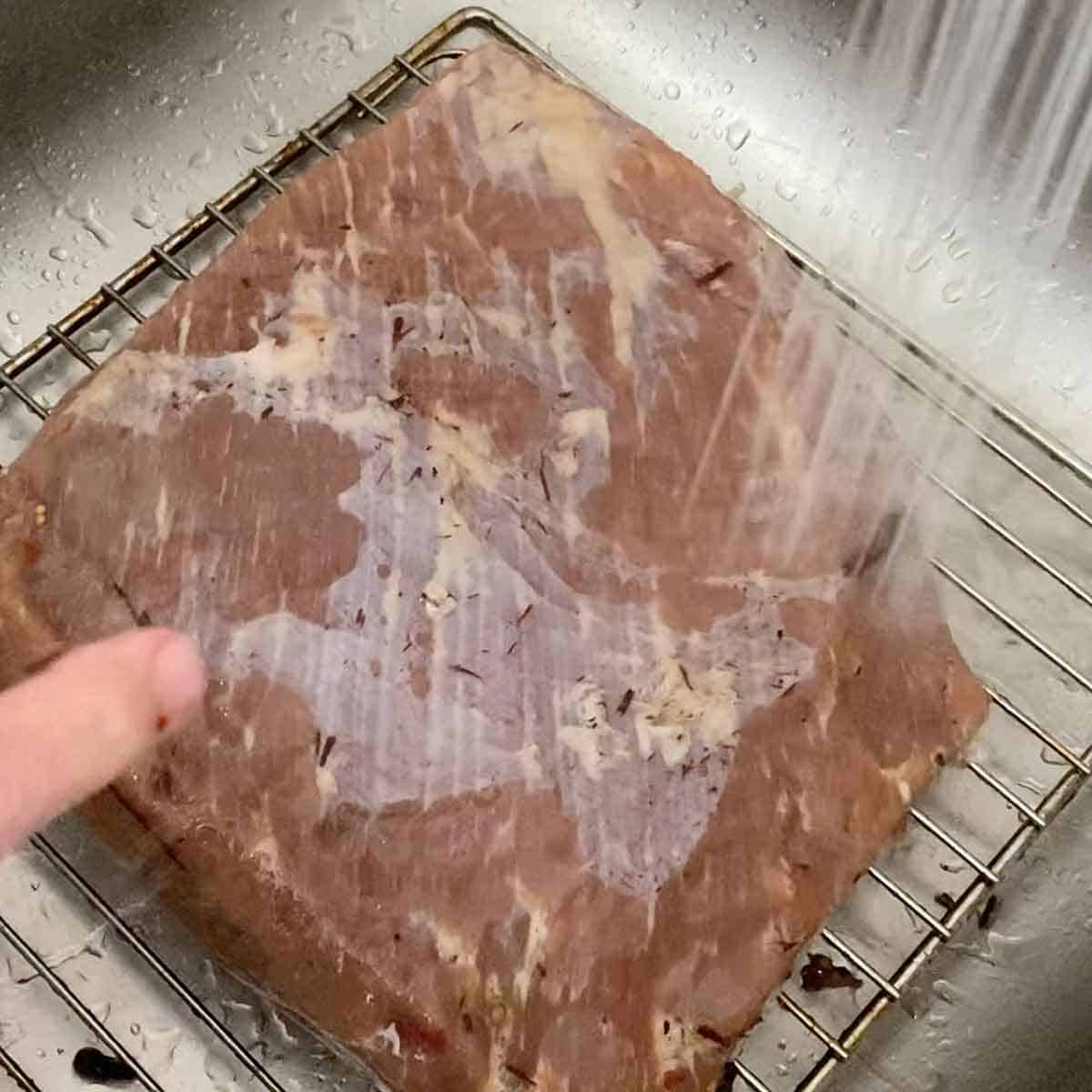 A person rinsing a brisket flat in a kitchen sink, the roast has been soaking in a curing brine for 1 week.