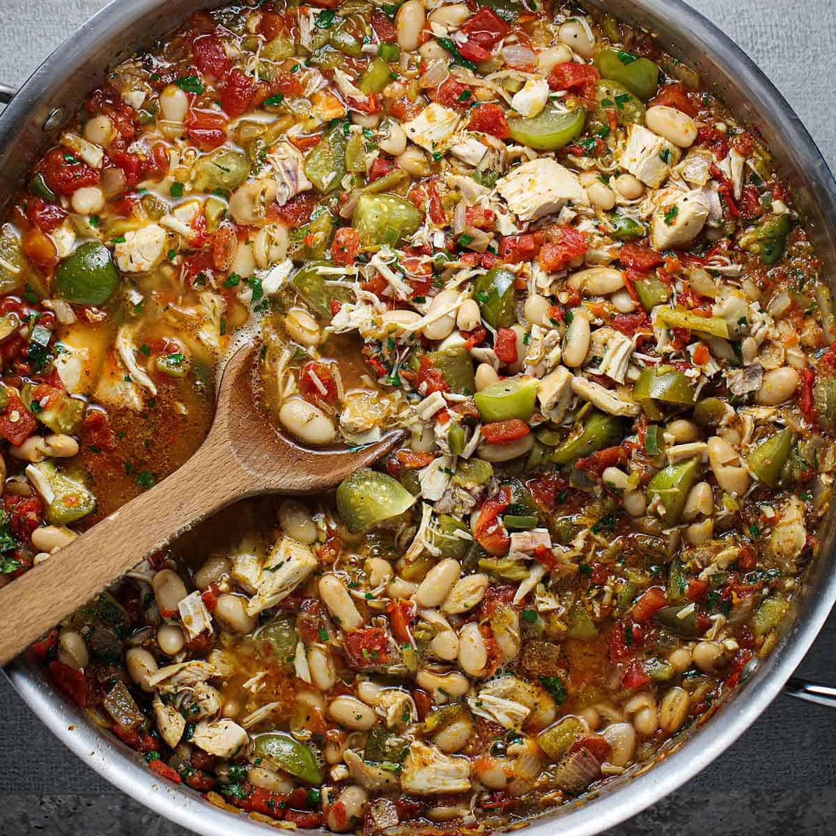 An overhead view of a large skillet filled with freshly prepared white chili with tomatillos and chicken.