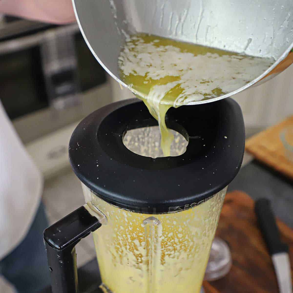 A person pouring melted butter through the top opening in the lid of a blender.