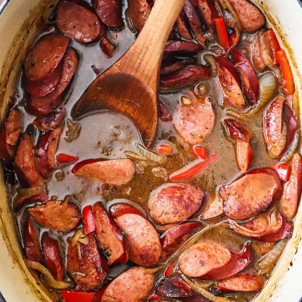 An overhead view of a large Dutch oven filled with simmering beer-braised kielbasa with peppers.