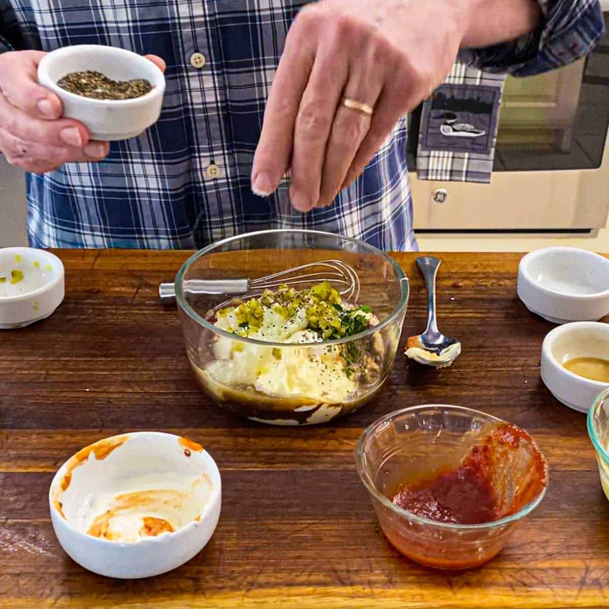A person sprinkling ground black pepper over the top of unmixed ingredients for homemade Russian dressing.