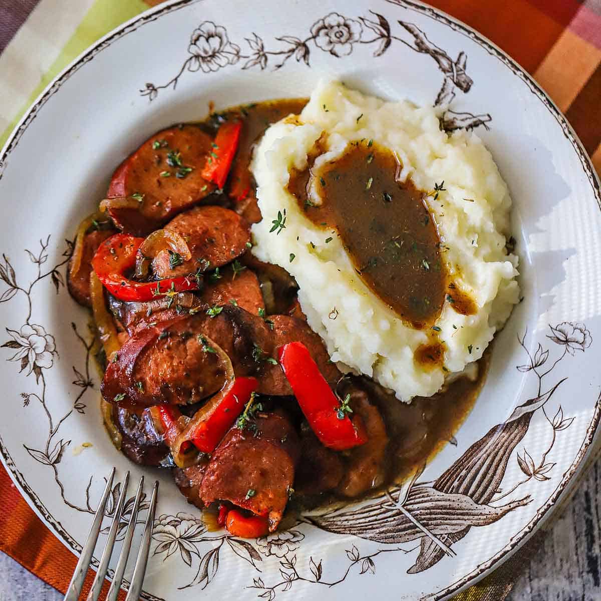 An overhead view of a vintage soup bowl filled with a serving of beer-braised kielbasa with peppers and mashed potatoes.