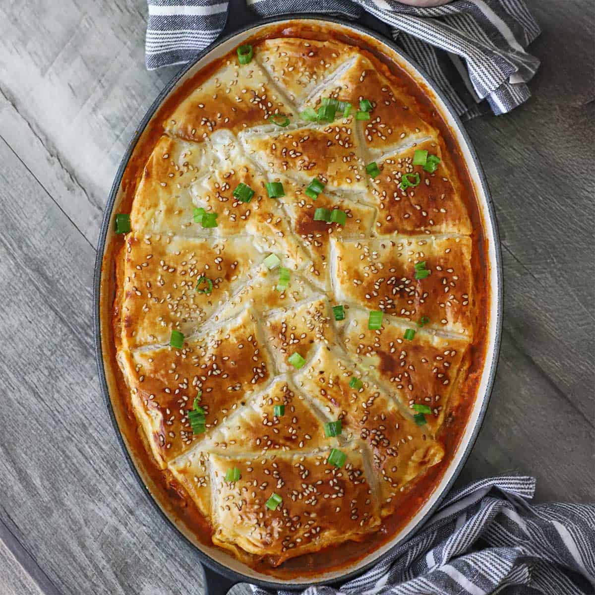 An overhead view of a freshly baked sloppy Joe casserole topped with golden brown puff pastry and sprinkled with toasted sesame seeds and chopped scallions.