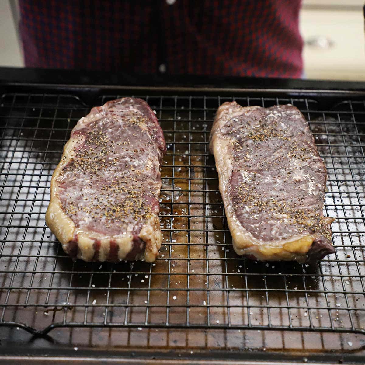 Two New York strip steaks that have been slow-cooked in an oven on a baking rack lined baking pan