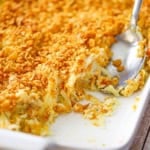 A close-up view of hashbrown casserole from scratch in a white baking dish with a portion of the casserole missing.