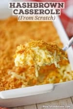 A person using a large spoon to raise a serving of hashbrown casserole from scratch from a large white baking dish.